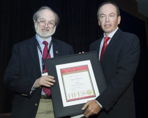 Two men, Gregg Vanderheiden and presenter, standing side-by-side, holding a plaque