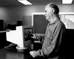 A man with a vision impairment is standing at a counter using a computer monitor.
