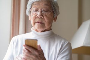 A senior woman peering down at the screen of a cell phone.